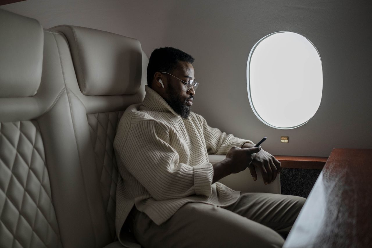 Services Bearded man in cozy sweater using smartphone on airplane, enjoying in-flight entertainment.
